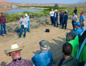 Much of the landscape around Shell would be arid without irrigation, like that supplied by the existing Leavitt Reservoir behind participants in the Wyoming Water Develoopment Office tour last week. Jason Mead, deputy director for the dam and reservoirs section, addresses the group. (Angus M. Thuermer Jr./WyoFile)