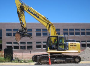 A backhoe operator prepares to bust and scoop up another section of sidewalk at Kelly Walsh High School in Casper. Construction worker Juan C. Avalos of Colorado died in a workplace accident at the construction site June 17, 2016. (Dustin Bleizeffer/WyoFile)