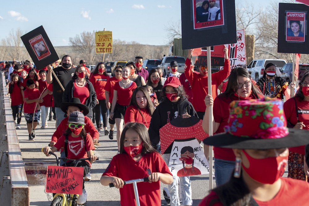 A sea of people wearing black and red and holding signs with people's faces and MMIP