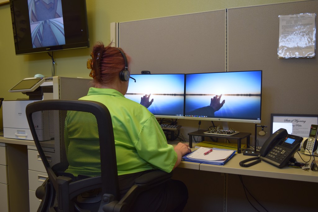 A woman at a desk with an earphone headset stares at two screens