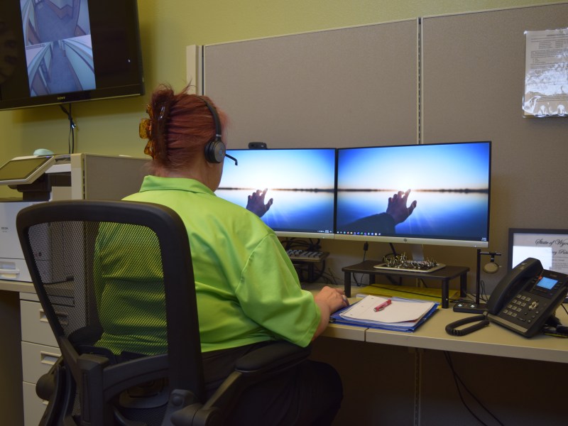 A woman at a desk with an earphone headset stares at two screens