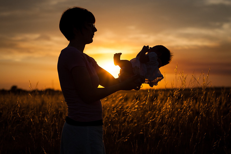 A silhouette of a woman holding a baby in a field at sunset