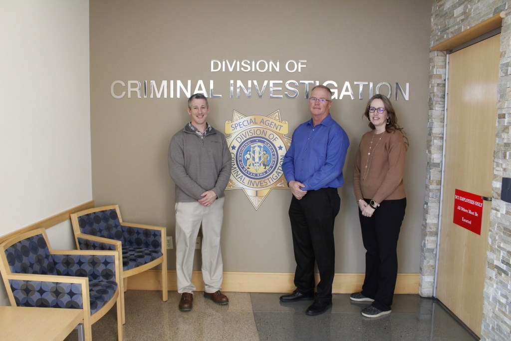 Three people stand in front of a sign that says Division of Criminal Investigation