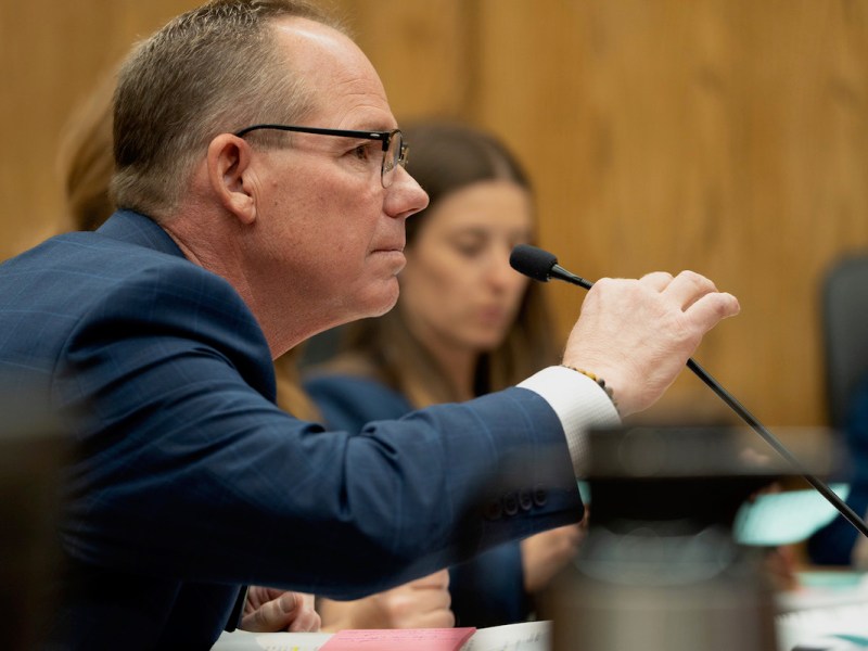 John Robinson, seated, leans into a skinny microphone on his desk in the courtroom