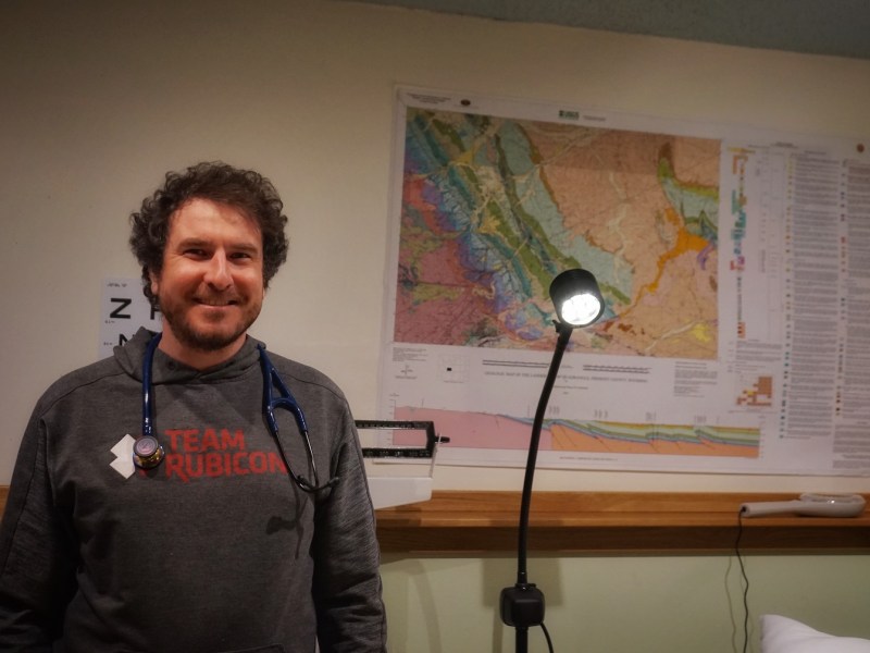 Kevin Wilson stands in front of a map of Wyoming with a stethoscope around his neck.