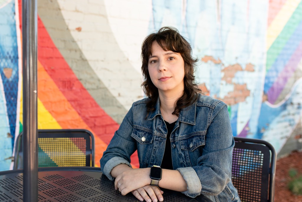 Ariel Bernath sits in front of a colorfully-painted brick building