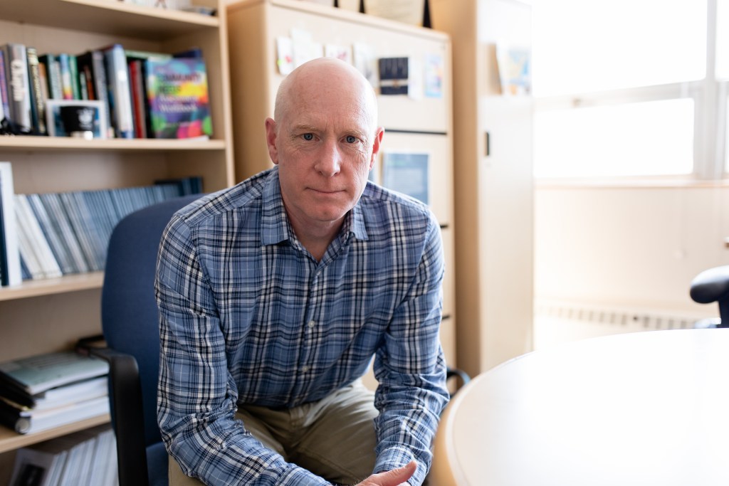 Rodney Wambeam sits in an chair in his office with books lining shelves behind him