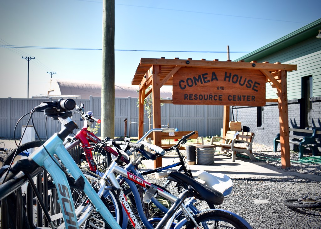 A full bike rack in front of a wooden sign that says "Comea House and Resource Center"