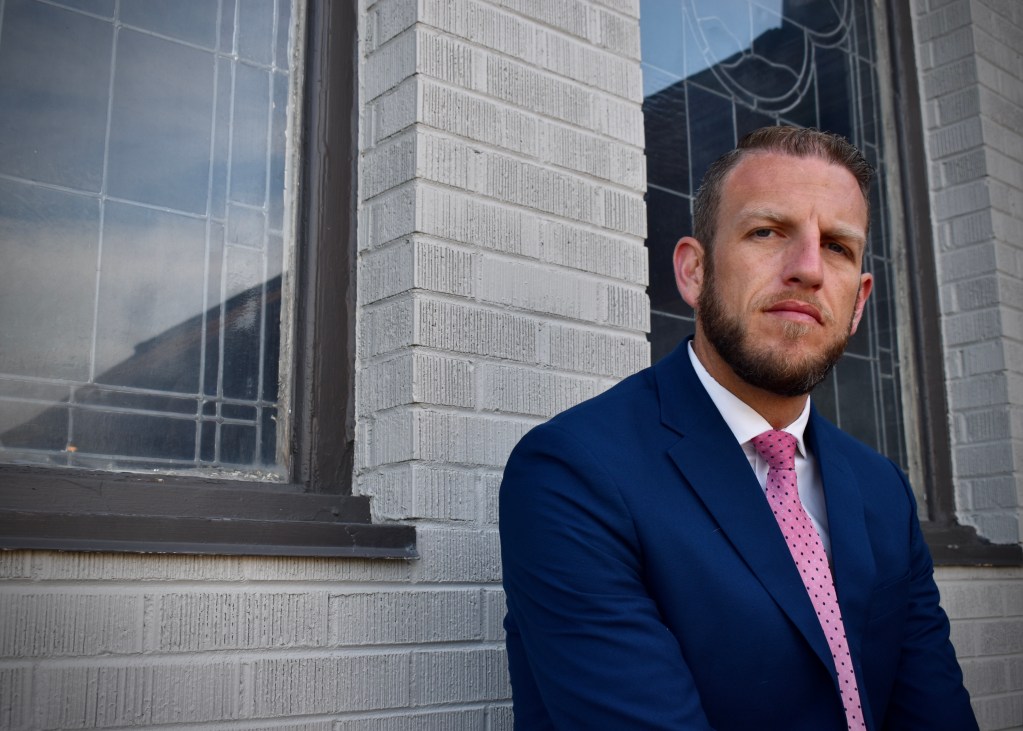 Levi Wardell sits in a suit and tie in front of the funeral home where he works