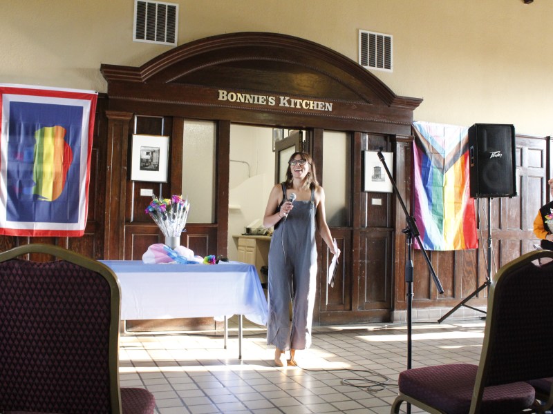 Rose Curtis stands in the train depot in Laramie with pride flags hanging on either side of her