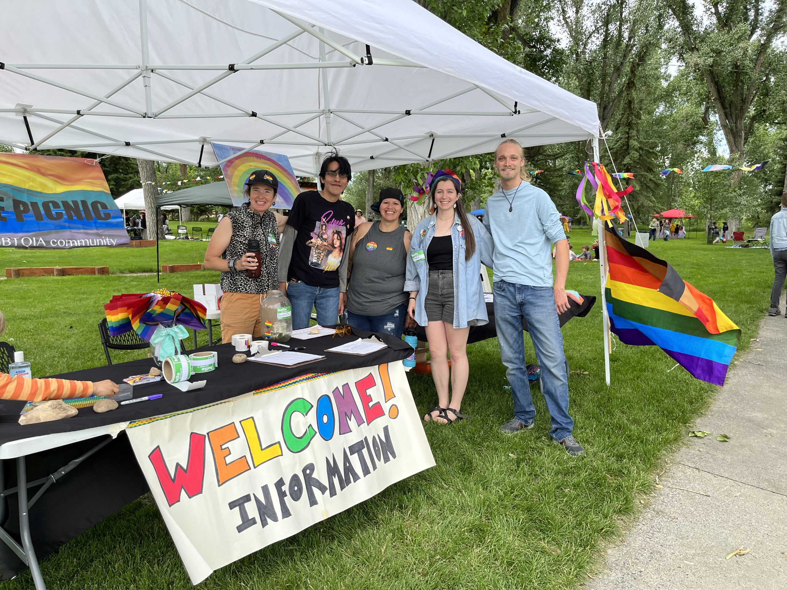 A group of five people stand behind a table adorned with a colorful sign that says "Welcome! Information"