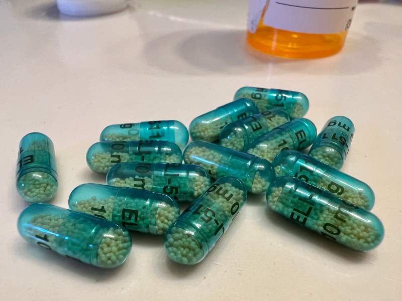 Clear pill capsules filled with tiny balls sit on a countertop