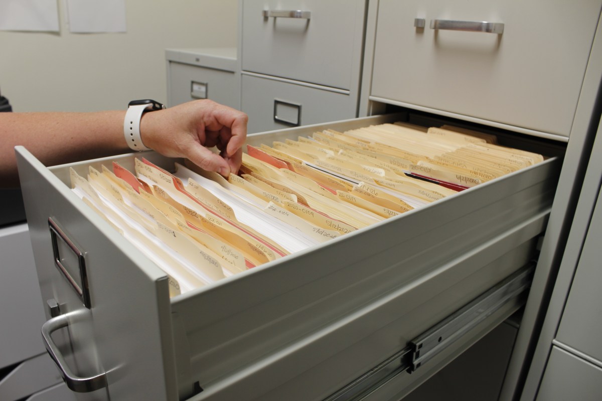 A hand over manilla folders in a metal filing cabinet
