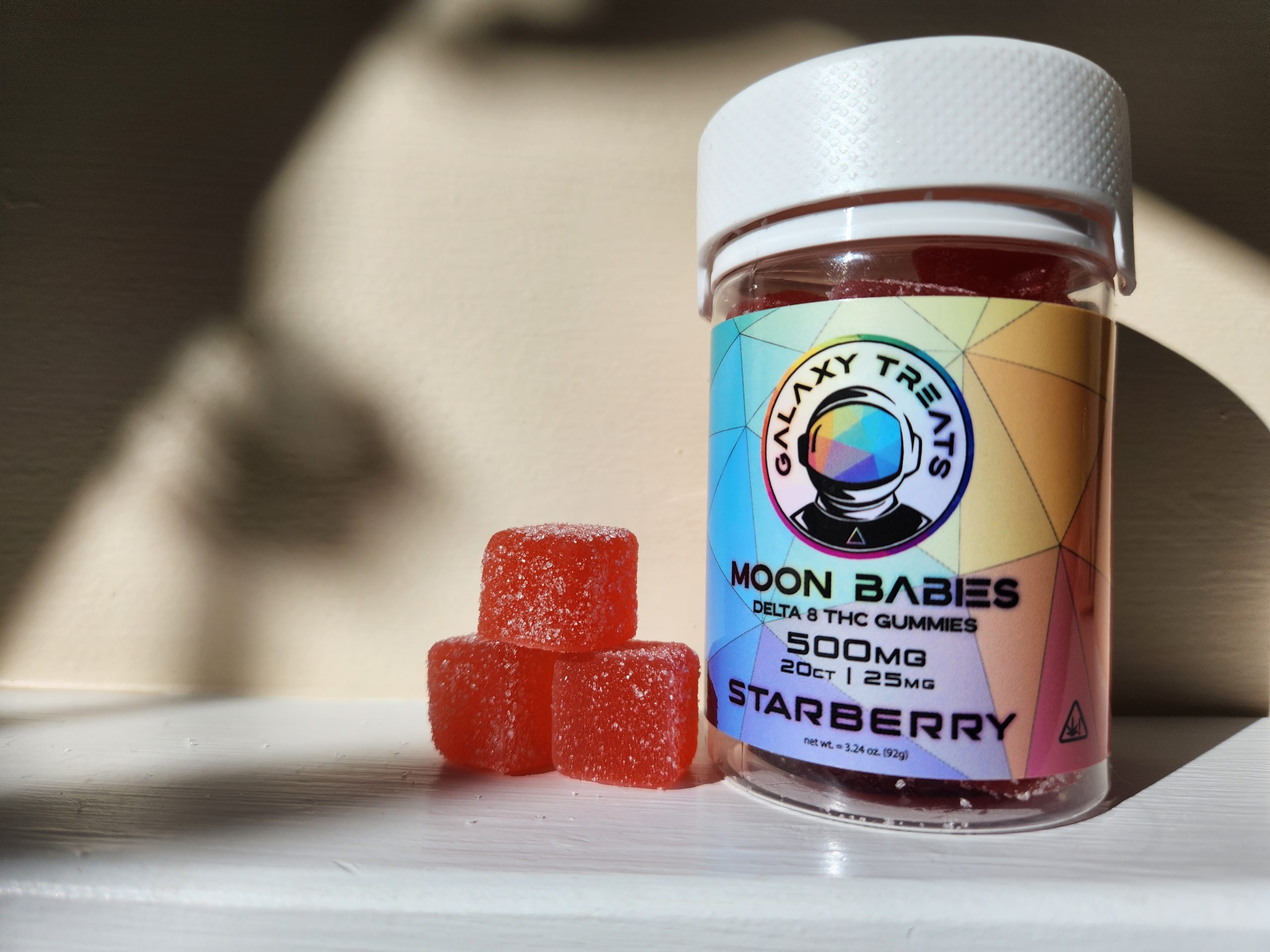 A bottle with chewy gummies that says Galaxy Treats, Moon Babies, Delta 8 THC Gummies, 500 MG, Starberry. Next to is a stack of three gummies.