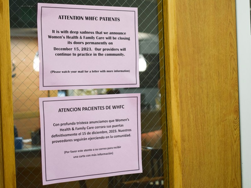 Signs hang on a door window telling WHFC patients that the office will close Dec. 15. One is in English, the other Spanish