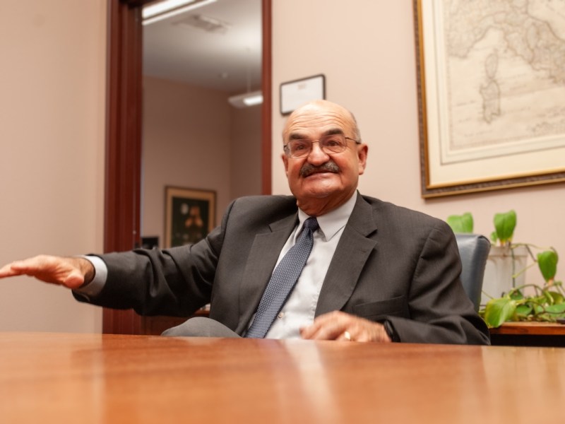 Kautz sits in a suit behind a table, holding out his hand as he talks