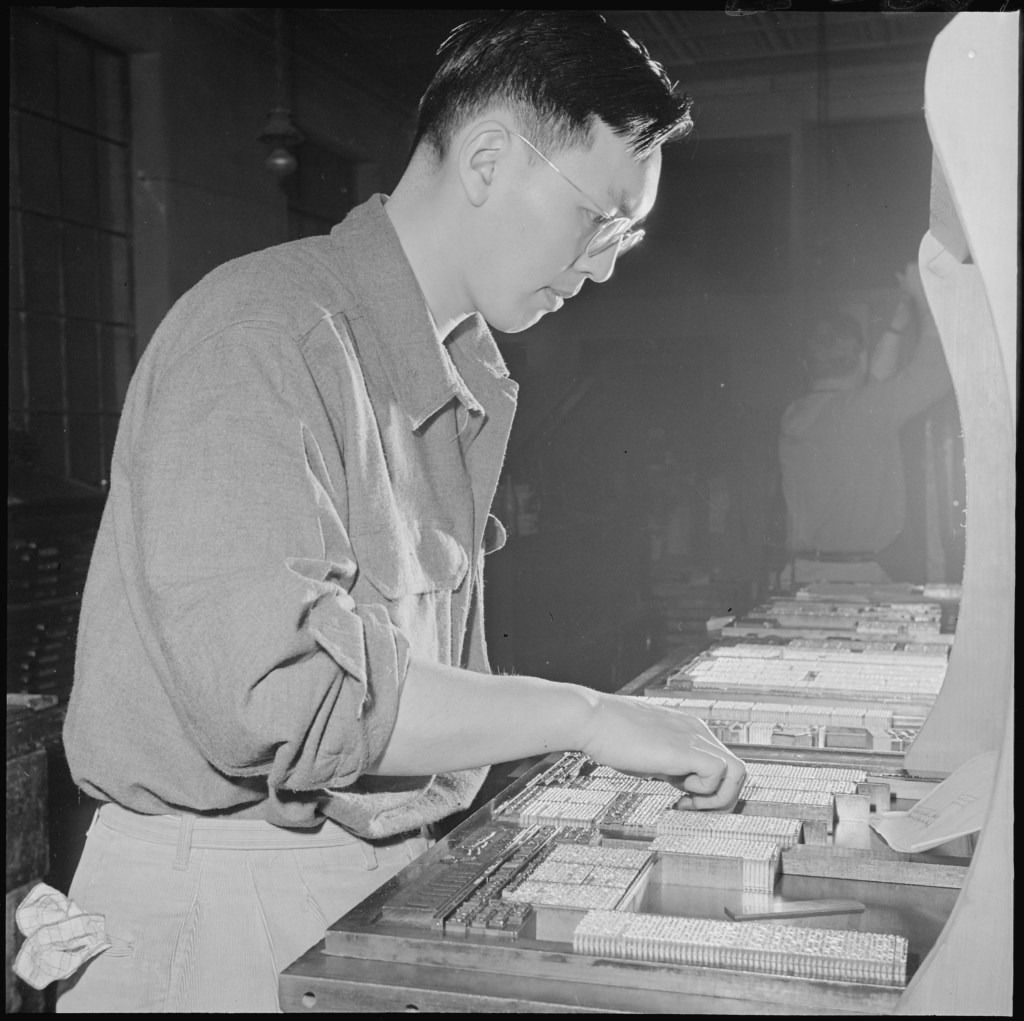A young man with glasses moves around printing press materials