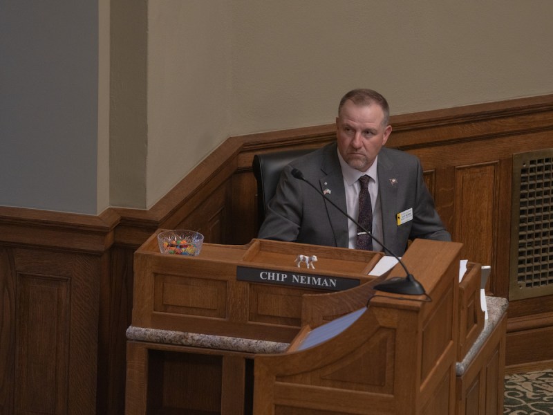 Neiman sits at his wooden desk on the House floor