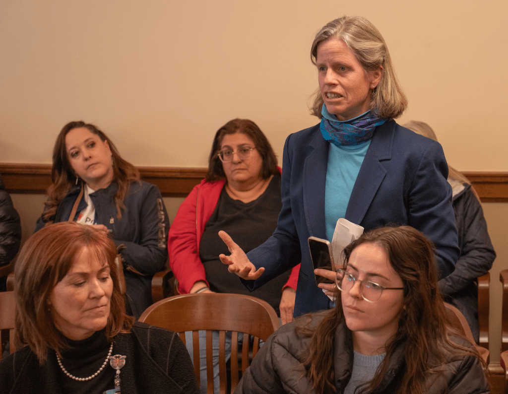 Christine stands by her chair in a committee meeting room at the capitol