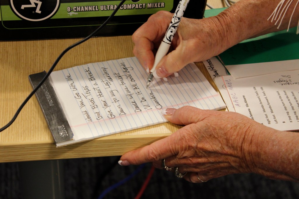 A hand writes song names on a notepad