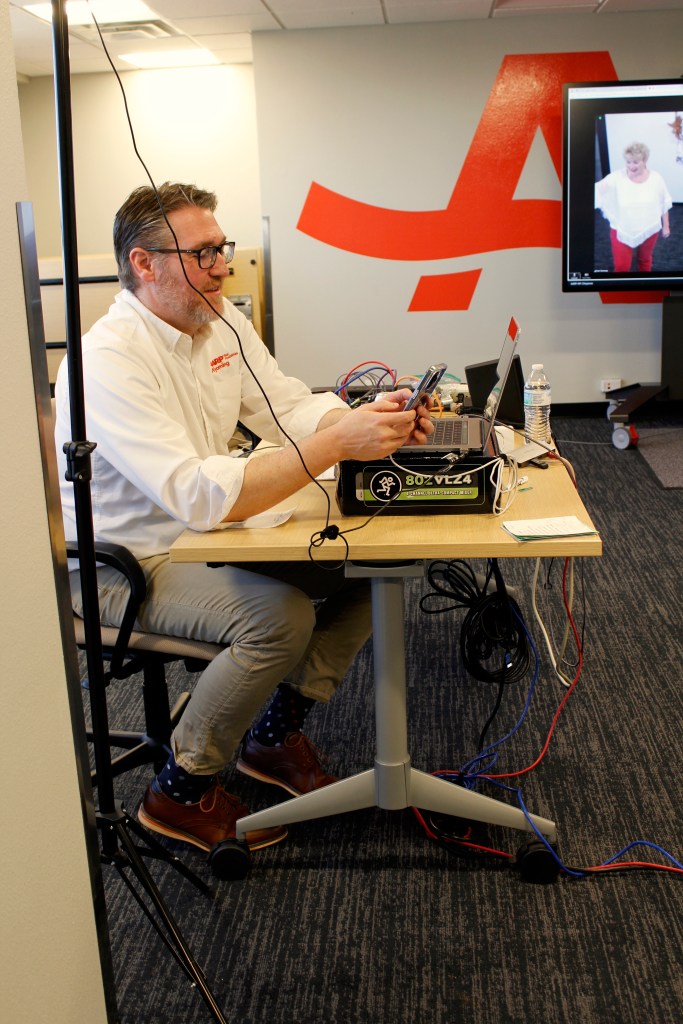 A man sits behind a table with wires, a sound board and a laptop