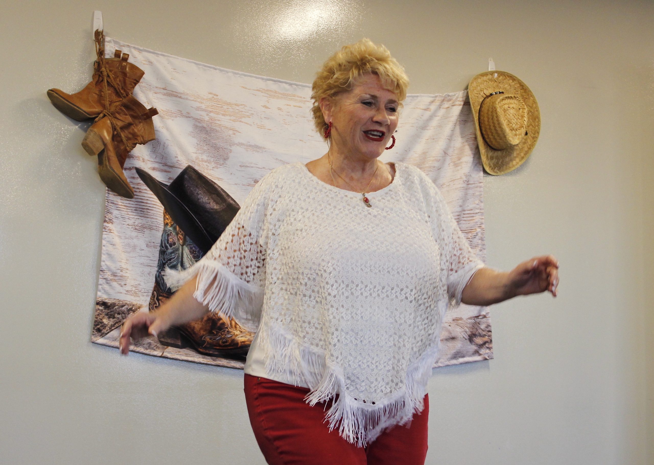 A woman dances in front of a wall that's adorned with cowboy boots and a cowboy hat