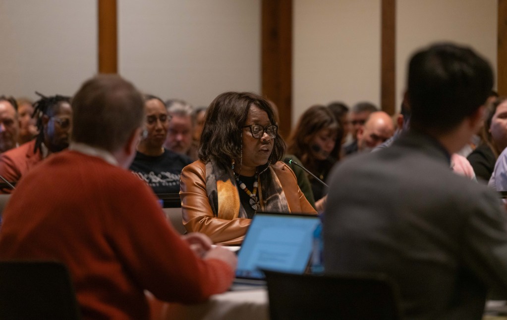 Camellia sits at a table before UW trustees, surrounded by a crowd