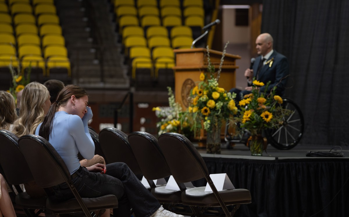 A woman near the stage cries into her hands while a man in a wheelchair talks on stage