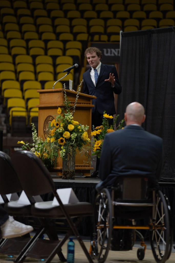 A young man in a suit talks into a microphone no stage