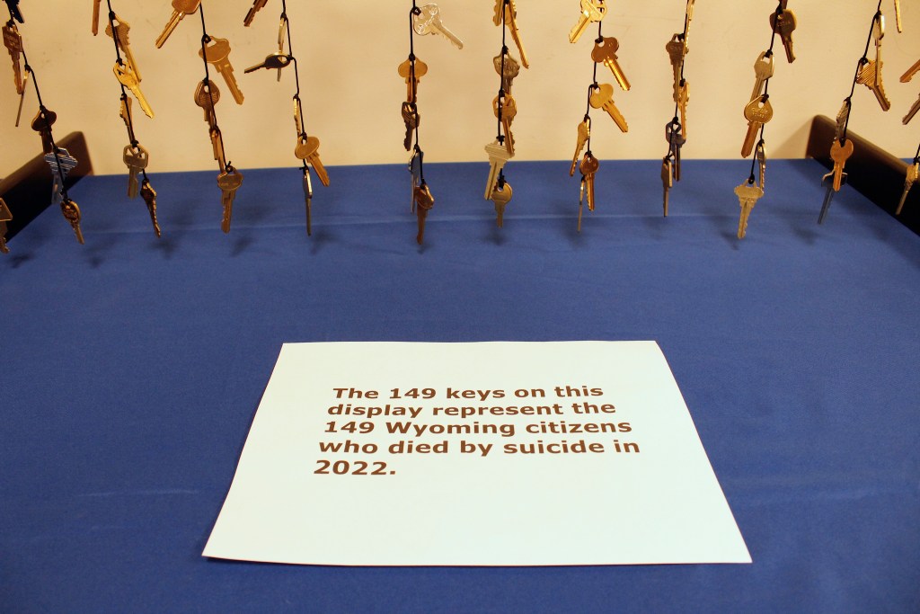 A sign says "the 149 keys on this display represent the 149 Wyoming citizens who died by suicide in 2022." Behind it are several strings of keys