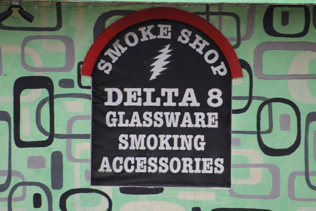A sign on the side of a building says smoke shop, delta 8, glassware, smoking, accessories