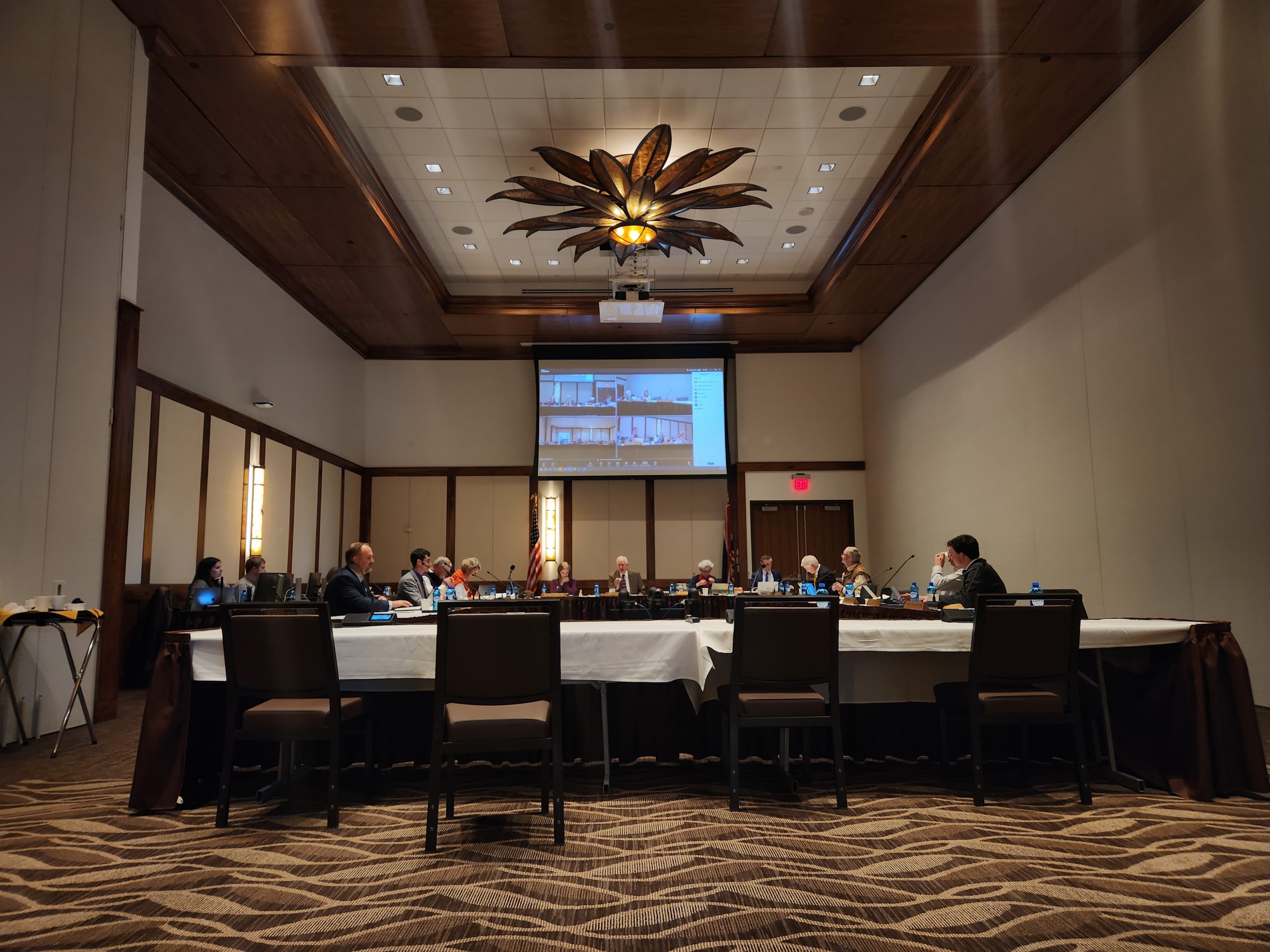 A large room with trustee members sitting around several large tables talking into little microphones