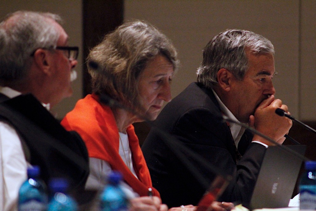 Three people sit at a table in front of small micriphones
