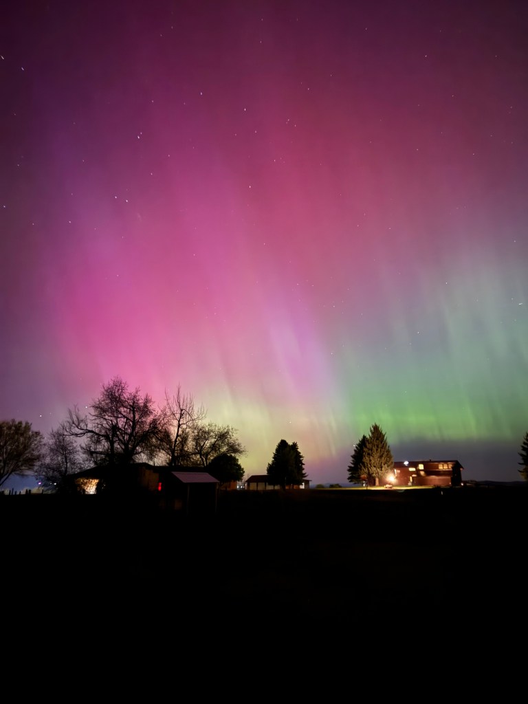 Northern lights over a house surrounded by dark fields