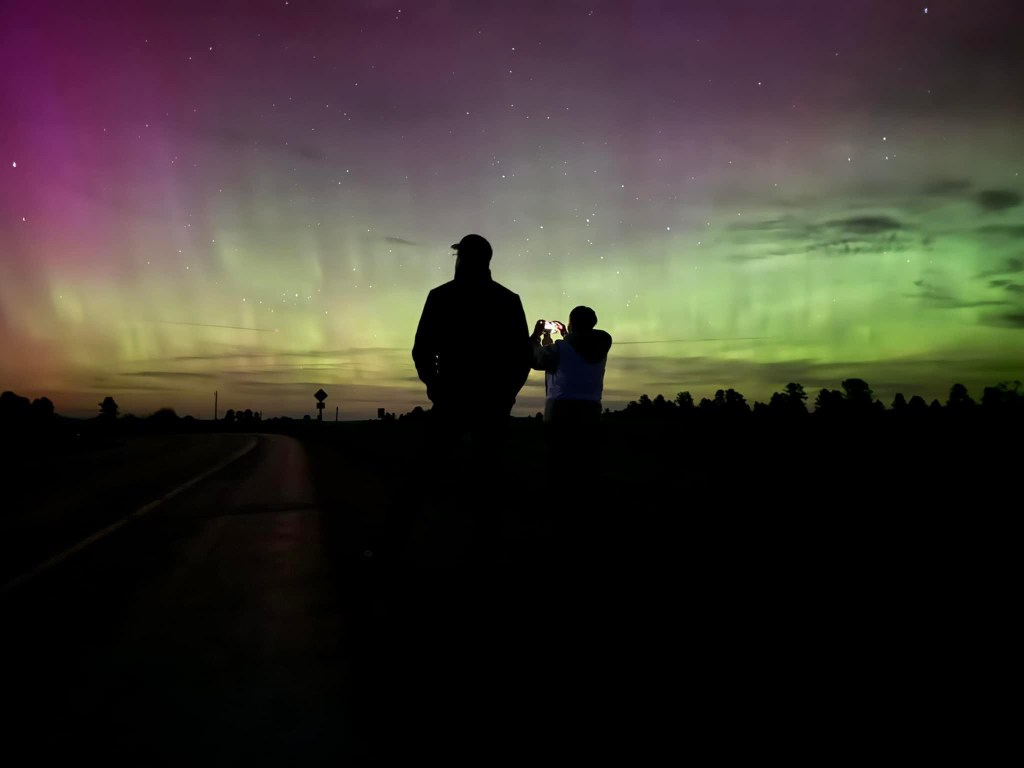 Two shadow figures stare out at the northern lights
