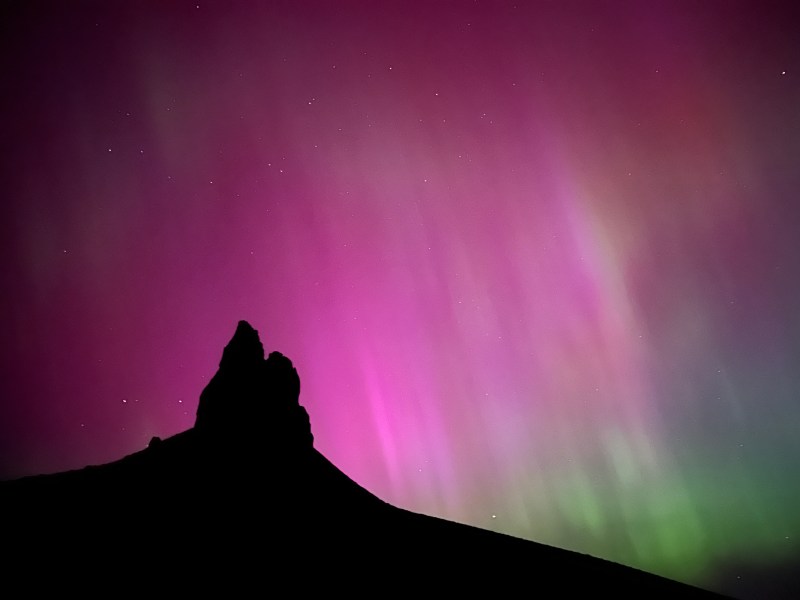 Pinks and green northern lights dance behind a rock outcropping