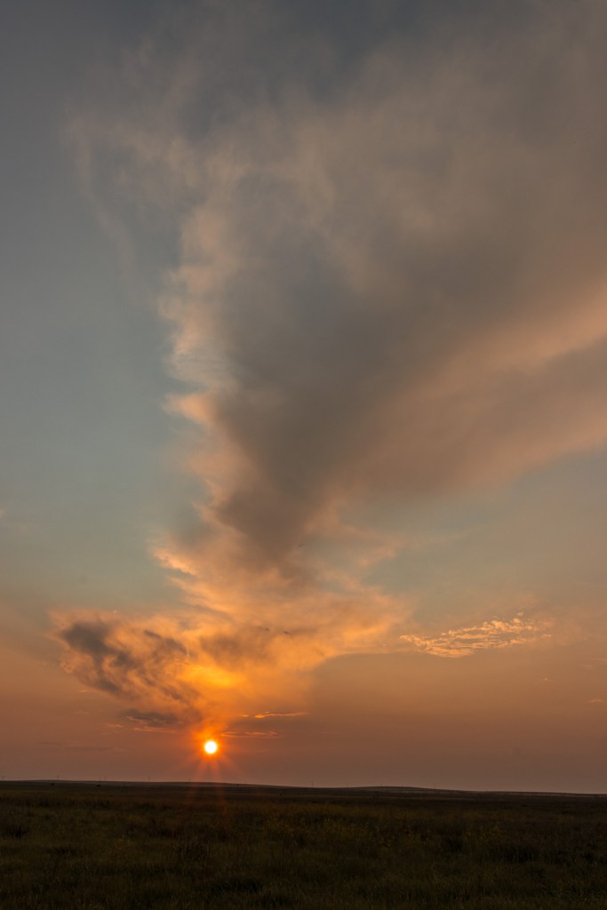 A line of clouds leads to an orange sunset on the horizon