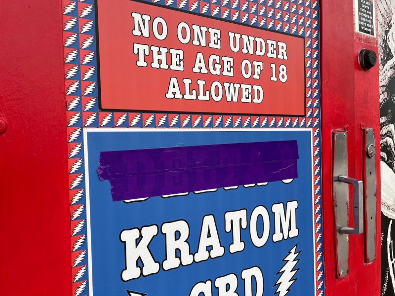 A sign that has delta-8 taped over in purple tape before listing other items for sale like CBD and Kratom