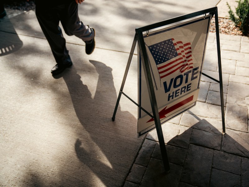 A vote sign with an arrow hangs on a stand while someone walks by it