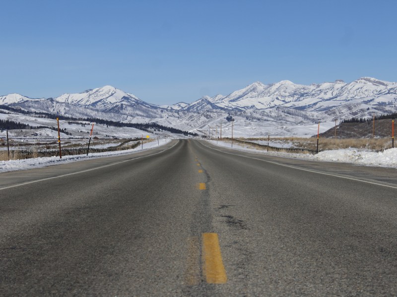 An image of a road with snow on either side and mountains in the distance
