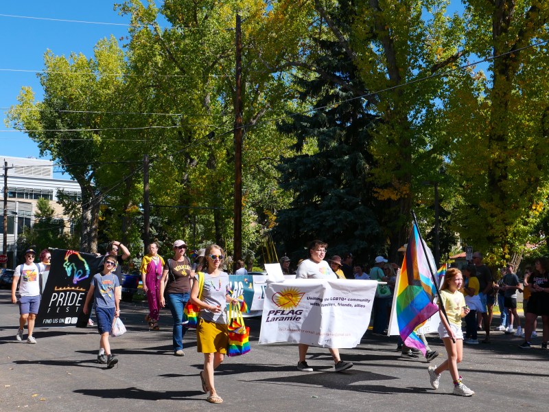 A group walk in a parade with pride flags and banners that say PFLAG Laramie and Laramie PrideFest