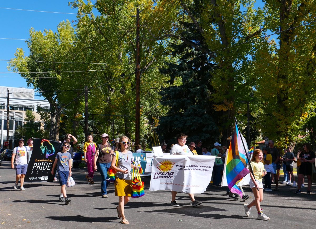 A group walk in a parade with pride flags and banners that say PFLAG Laramie and Laramie PrideFest