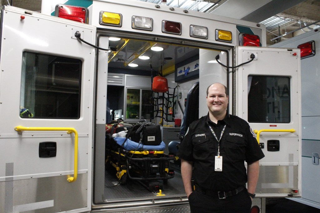 A man stands in front of open back doors of an ambulance