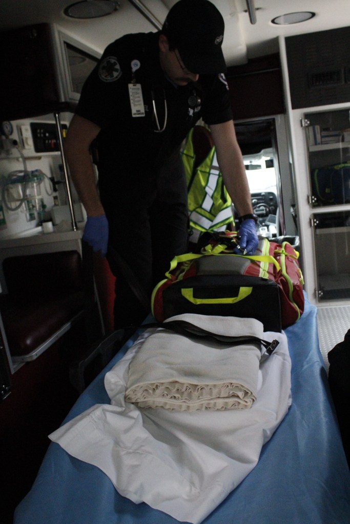 A man holds a bundle on a gurney in the back of an ambulance