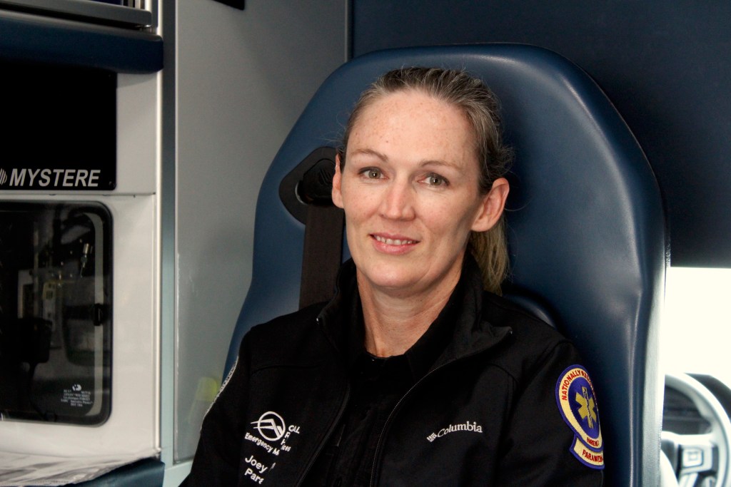 A woman sits in the back of an ambulance, strapped into a chair