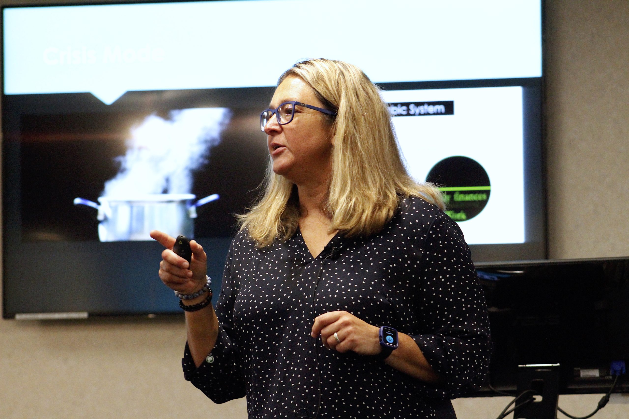 A woman at the front of a classroom with a picture behind her of a boiling pot
