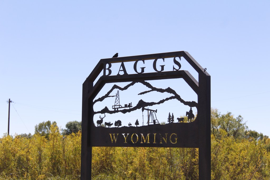 A sign that says Baggs Wyoming with a mountain scene