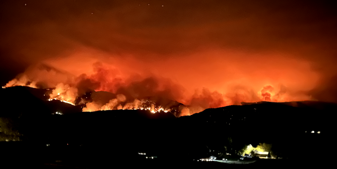 The orange and red haze of a massive fire burning over a hilltop at night