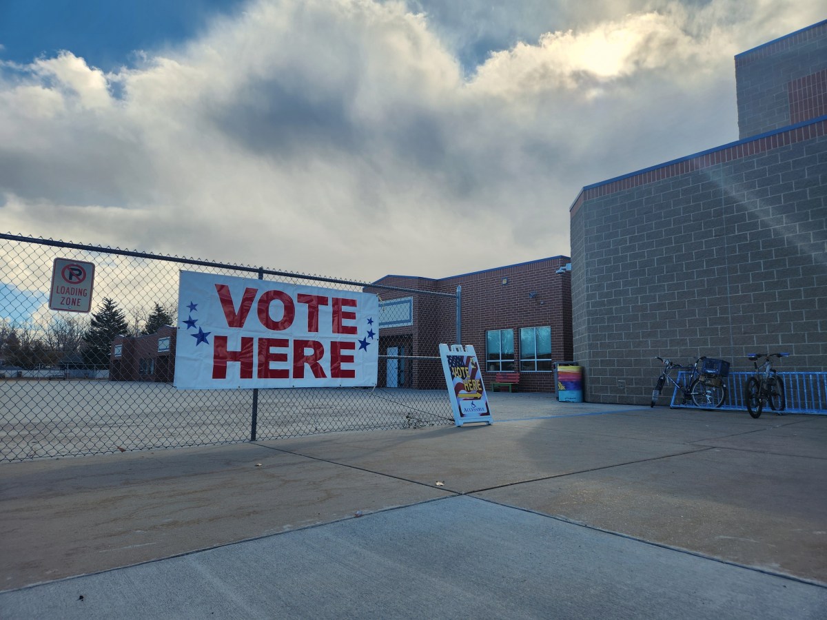 Two "Vote Here" signs in front of a brick building